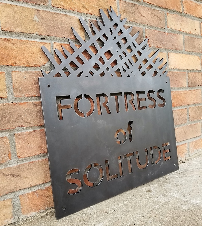 May include: A metal sign with a geometric design at the top and the words "Fortress of Solitude" in a stencil font.