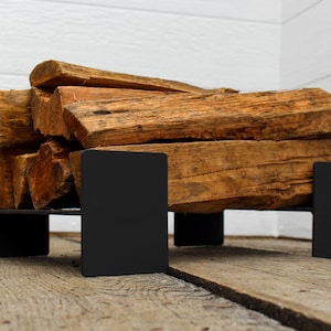 May include: A black metal firewood rack with stacked pieces of firewood. The rack is sitting on a wooden floor.
