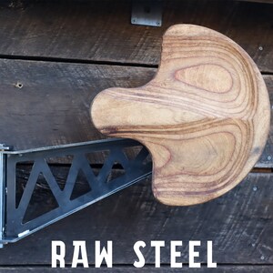 May include: A wooden wall-mounted stool with a unique curved seat and a black metal bracket. The bracket is attached to the wall with screws and has a triangular design. The text "RAW STEEL" is printed on the wall below the stool.