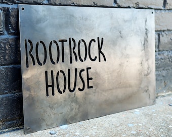 May include: A metal sign with the words "ROOTROCK HOUSE" cut out in a stencil style.