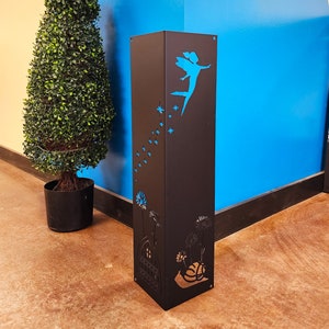 May include: Black metal garden stake with a cutout design of a fairy flying with stars and flowers. The stake is against a blue wall.