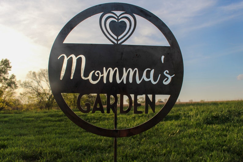 May include: A black metal garden sign with a heart design and the text "Momma's Garden".