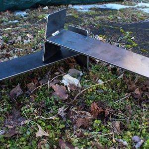 May include: Two metal stands made of steel, with a black finish, are stacked on top of each other. The stands are sitting on a bed of green moss and brown leaves.