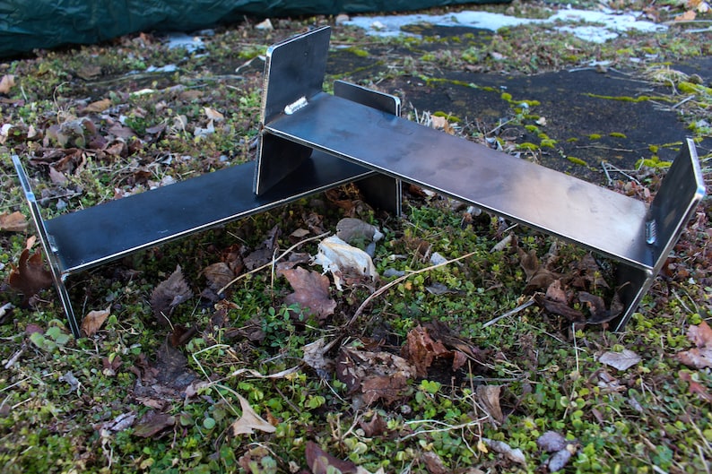 May include: Two metal stands made of steel, with a black finish, are stacked on top of each other. The stands are sitting on a bed of green moss and brown leaves.