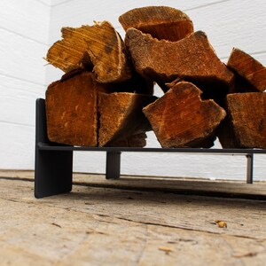 May include: A black metal firewood rack with stacked pieces of firewood. The rack is sitting on a wooden surface.