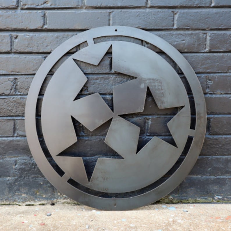 K&ouml;nnte beinhalten: Eine Wanddekoration aus Metall mit dem Logo des Bundesstaates Tennessee, einem Kreis mit drei Sternen darin. Das Logo ist aus dem Metall ausgeschnitten und hat einen rustikalen, abgenutzten Look.