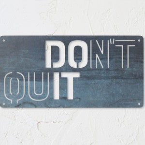 May include: A blue metal sign with the words "DON'T QUIT" in white cutout letters.