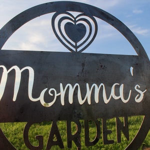 May include: A metal sign with a heart cut out in the top and the words "Momma's Garden" in white lettering.