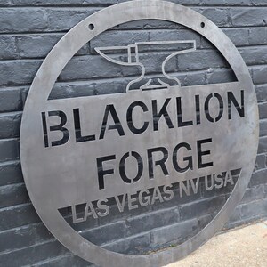 May include: A circular metal sign with a cut-out design. The sign features the text "BLACKLION FORGE LAS VEGAS NV USA" and a stylised image of an anvil.