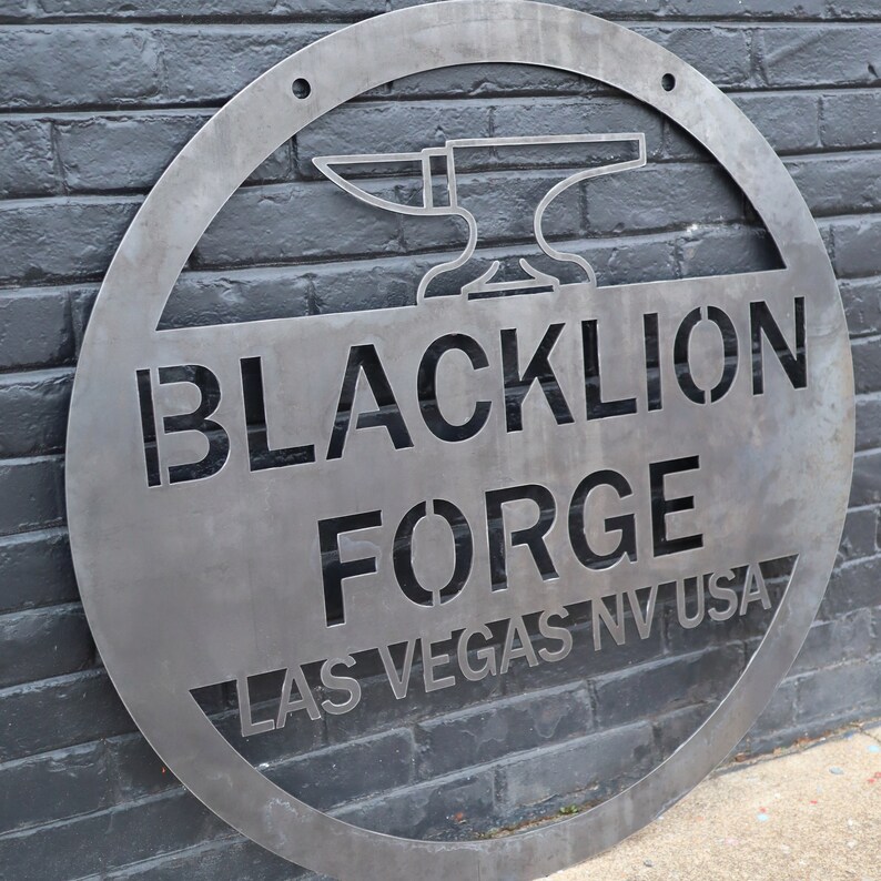 May include: A circular metal sign with a cut-out design. The sign features the text "BLACKLION FORGE LAS VEGAS NV USA" and a stylised image of an anvil.