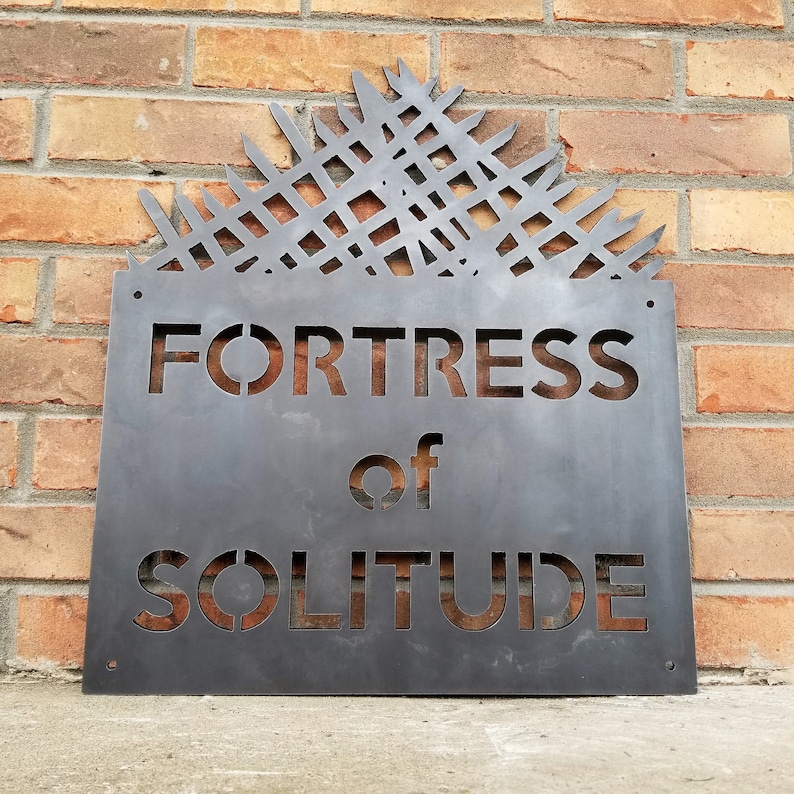 May include: A metal sign with a distressed finish, featuring a geometric design and the text "Fortress of Solitude".