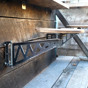May include: A black metal bar with a triangular pattern is mounted to a wooden wall. A wooden shelf is attached to the bar, which can be adjusted up and down.