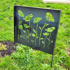 May include: A black metal garden screen with a cut-out design of poppy flowers. The screen is standing upright in a grassy area.