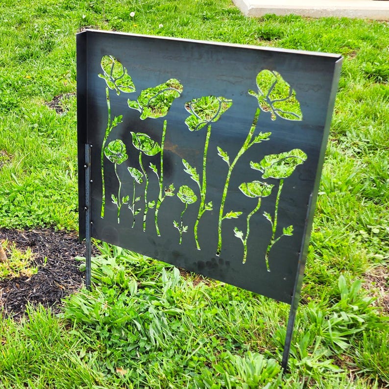 May include: A black metal garden screen with a cut-out design of poppy flowers. The screen is standing upright in a grassy area.