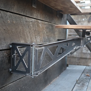 Puede incluir: Una barra de metal con un dise&ntilde;o triangular est&aacute; montada en una pared de madera. La barra sostiene un taburete de bar de madera con un mecanismo giratorio de metal.
