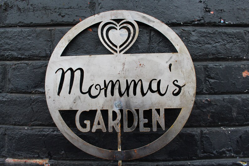 May include: A metal sign with a heart design and the text "Momma's Garden" in a circular shape.