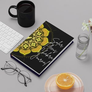 May include: A black journal with a yellow and gold mandala design on the cover. The text "Solar Plexus Chakra Journal" is written in white on the cover.
