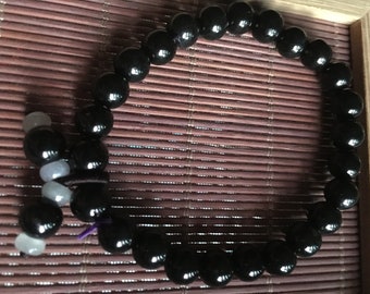 May include: A black beaded bracelet with a knotted closure and a small strand of white beads attached.
