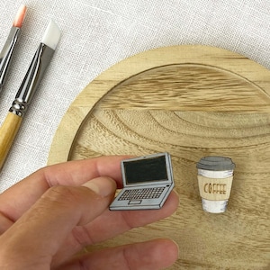 Könnte beinhalten: Zwei Holz-Pins, einer zeigt einen Laptop und der andere eine Kaffeetasse mit dem Wort "Coffee" darauf. Die Pins befinden sich auf einer Holzoberfläche.