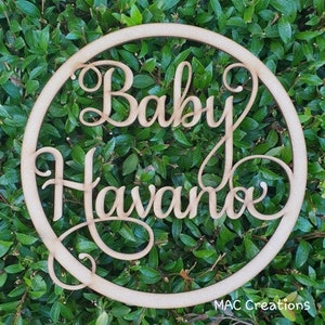 May include: Wooden circle with the words "Baby Havano" written in a cursive font. The circle is surrounded by green foliage.