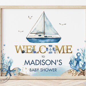 May include: A blue and white sailboat with a lifebuoy and anchor, surrounded by seashells and seaweed. The text "Welcome to Madison's Baby Shower" is written in gold lettering.