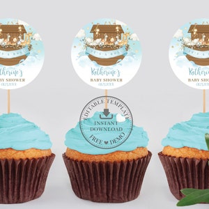 May include: Three blue and brown cupcakes with a round, white, and gold cupcake topper featuring a cartoon illustration of Noah's Ark with animals. The topper says "It's a Boy" and "Katherine's Baby Shower" with a date.