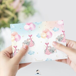 May include: A pink and blue patterned card with a repeating design of gray elephants holding onto pink and yellow balloons. The elephants are wearing pink party hats and there are gold stars and clouds in the background. The text "Lil' The Happy Cat Studio" is at the bottom of the card.