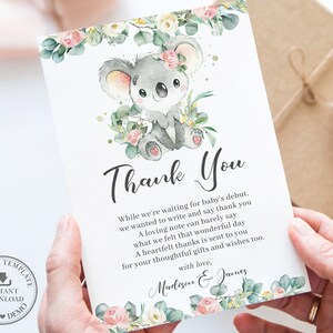 May include: A baby shower thank you card featuring a watercolor illustration of a gray koala bear surrounded by flowers and greenery. The card includes the text "Thank You" and a personalized message.