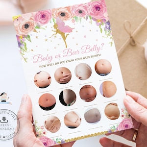 May include: A printable baby shower game card with the text "Baby or Beer Belly?" and illustrations of baby bumps. The card is decorated with floral and fairy graphics in pink, gold, and purple. The card is held by a person.