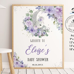 Op de afbeelding: Een ingelijst babyborrelbord met een aquarelontwerp. Een grijze koala rust op een zilveren glittermaan, omringd door paarse rozen en groen. Het bord leest "Welcome to Eloise's Baby Shower" met de datum 08.26.20XX. Printmaten: 23x30, 30x41, 38x51, en 46x61 cm.