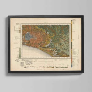 May include: Framed vintage map print featuring a detailed topographical view with a coastal region. The map displays a range of colors, including brown, green, and blue, and is encased in a black frame. The map is a vintage style print.