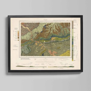 May include: Framed vintage map print with a detailed geological illustration. The map features a variety of colors, including greens, browns, and yellows, depicting terrain and geological features. The print is encased in a black frame, suitable for home or office decor.
