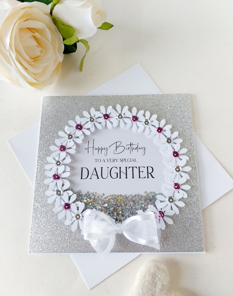Peut inclure: Une carte de v&oelig;ux argent&eacute;e &agrave; paillettes avec une couronne de marguerites blanches et un n&oelig;ud blanc. La carte dit "Joyeux anniversaire &agrave; une fille tr&egrave;s sp&eacute;ciale".