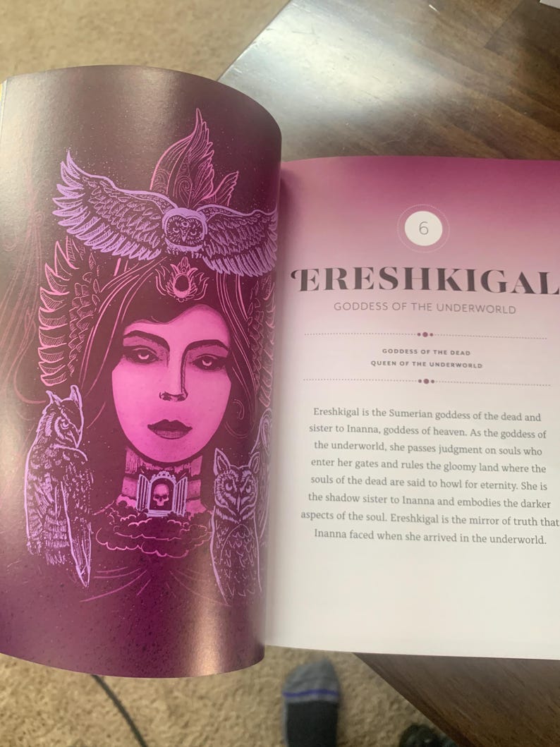 Pode incluir: Uma p&aacute;gina de livro aberta exibe uma ilustra&ccedil;&atilde;o de Ereshkigal, a deusa sum&eacute;ria do submundo. A imagem apresenta uma mulher com rosto rosa, adornada com um cocar de coruja e duas corujas. O texto descreve a deusa.