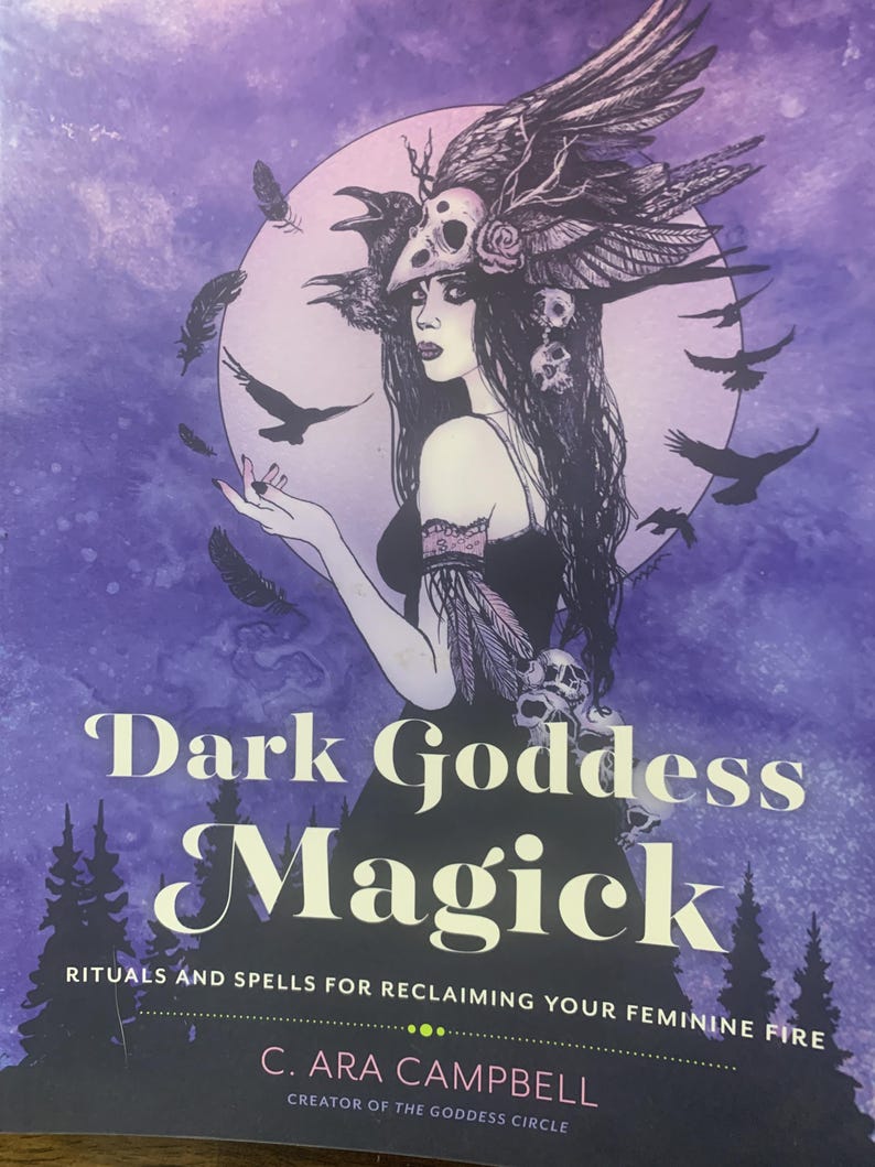 Pode incluir: Capa de livro com o t&iacute;tulo "Dark Goddess Magick" em branco. A capa apresenta uma ilustra&ccedil;&atilde;o de uma mulher com cabelo escuro e um adorno de cabe&ccedil;a, rodeada por corvos e penas, sobre um fundo roxo. A autora &eacute; C. Ara Campbell.
