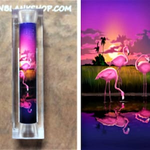 May include: A clear acrylic pen blank with a colorful image of pink flamingos standing in a body of water at sunset. The image is printed on a clear background and is visible from all sides of the pen blank.
