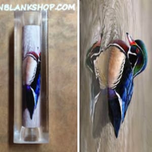 May include: A wooden pen blank with a colorful image of a wood duck. The image is of a wood duck with its head turned to the side, showing its colorful plumage. The pen blank is approximately 6 inches long and 1 inch in diameter. The image is clear and vibrant.
