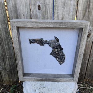 May include: A framed artwork featuring a mosaic of small, dark grey stones arranged in the shape of the state of Florida.