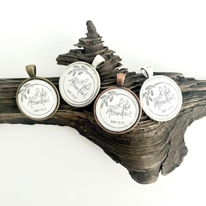 May include: Three silver, copper, and bronze pendants with a white background and black lettering that reads "Life Abundant John 10:10". The pendants are on a piece of driftwood.