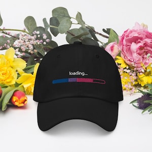 Peut inclure: Une casquette de baseball noire avec une barre de progression brodée en blanc qui indique "chargement..." avec des couleurs bleu, violet et rouge.