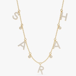 May include: A gold necklace with five charms, each featuring a letter of the alphabet set with small diamonds. The letters are "S", "A", "R", "A", and "H".