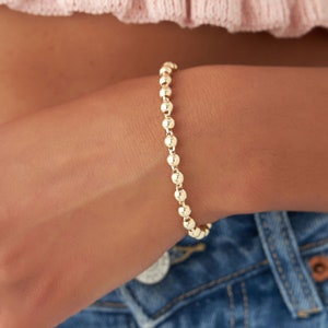 May include: A gold beaded bracelet with a simple design. The bracelet is made of small, round beads that are evenly spaced.
