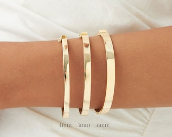 Puede incluir: Tres pulseras de oro de diferentes anchos, 4 mm, 5 mm y 6 mm, se muestran en la muñeca de una persona.