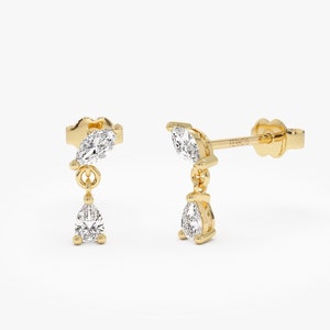May include: A pair of gold earrings with a pear-shaped diamond dangling from a marquise-shaped diamond.