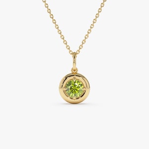 May include: A gold-colored necklace with a round pendant featuring a light green gemstone. The pendant is encircled by a gold bezel and hangs from a delicate gold chain. The gemstone has a faceted appearance.