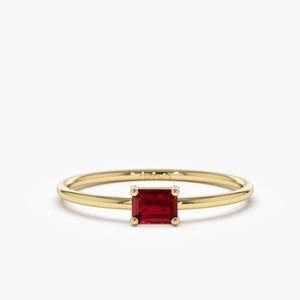 May include: A simple gold band ring with a red emerald-cut gemstone.