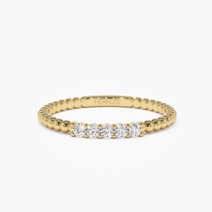 May include: A delicate gold band ring with a row of five small round diamonds set in the center. The band is beaded and has the inscription "FERKOS" on the inside.