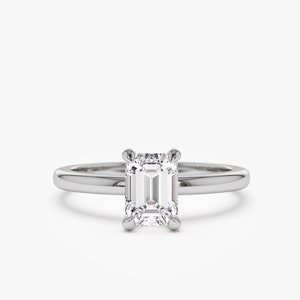 May include: A solitaire engagement ring with an emerald-cut diamond. The diamond is set in a four-prong setting on a thin, polished silver band. The ring is displayed against a white background.