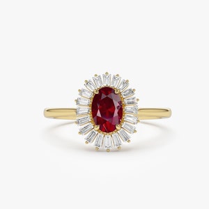 Puede incluir: Un anillo de oro con una piedra preciosa ovalada de rubí rojo rodeada por un halo de diamantes más pequeños de forma baguette.