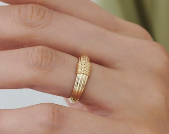 May include: A gold-toned ring with a woven design. The ring is worn on a finger.